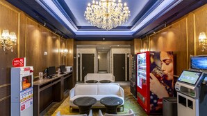 Un hall d’hôtel avec un lustre, un canapé, deux petites tables, un distributeur automatique et un défibrillateur automatisé externe (DAE).