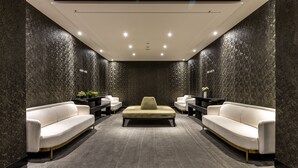 Un hall d’entrée moderne avec deux canapés blancs, un pouf central et un mur texturé de couleur sombre.