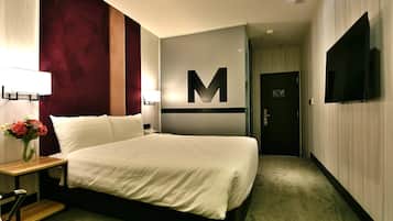 A hotel room with a large bed, a desk with a lamp, a vase of flowers, and a television on the wall.