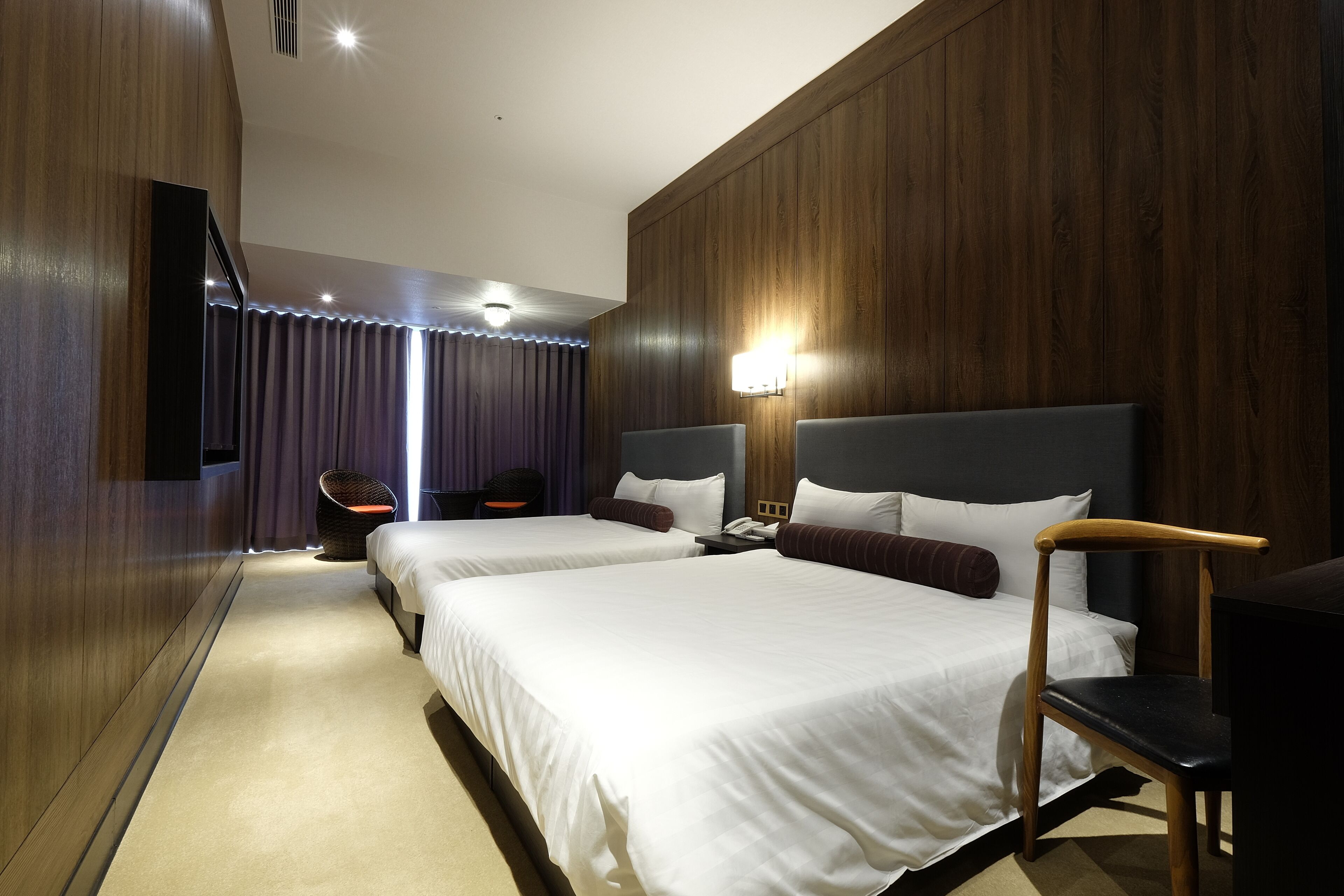 A hotel room with two beds, a desk, a chair, and a television.