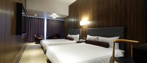 A hotel room with two beds, a desk, a chair, and a television.