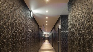 Un long couloir étroit aux murs sombres et à la texture marquée, dont le sol est recouvert d’une moquette, et qui mène à une porte portant l’inscription 4019-40.