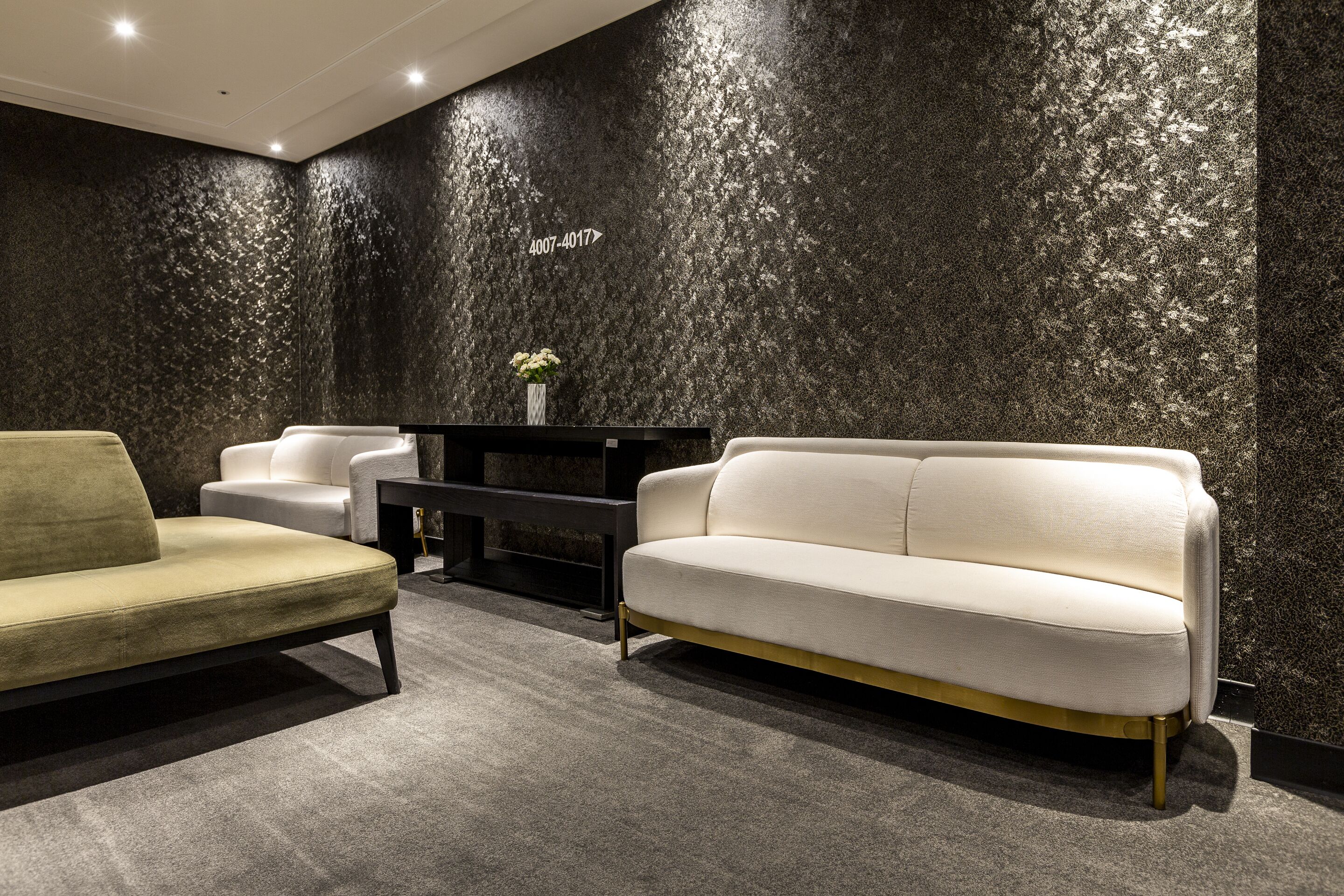 Eine moderne Lobby mit einer dunkel strukturierten Wand, einem weißen Sofa, einem grünen Sessel und einem schwarzen Beistelltisch mit Blumenvase.