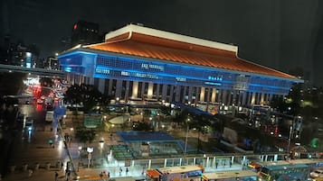 A large, modern building with a prominent entrance and multiple levels, surrounded by a busy urban street with vehicles and pedestrians.