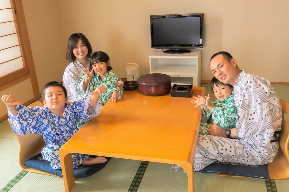 Une pièce avec un sol recouvert de tatamis, une petite table en bois, un téléviseur posé sur un meuble et un paravent japonais traditionnel.
