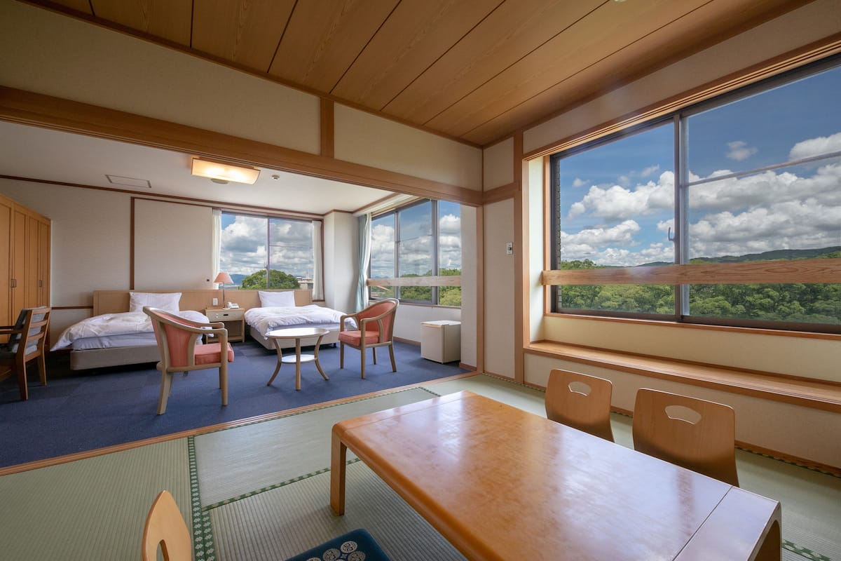 Une chambre d’hôtel avec une grande fenêtre, un lit, un bureau et une chaise.