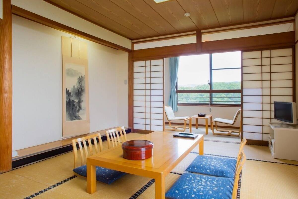 Une pièce de style japonais traditionnel, avec un sol recouvert de tatamis, une petite table basse entourée de coussins, une porte coulissante et un téléviseur.