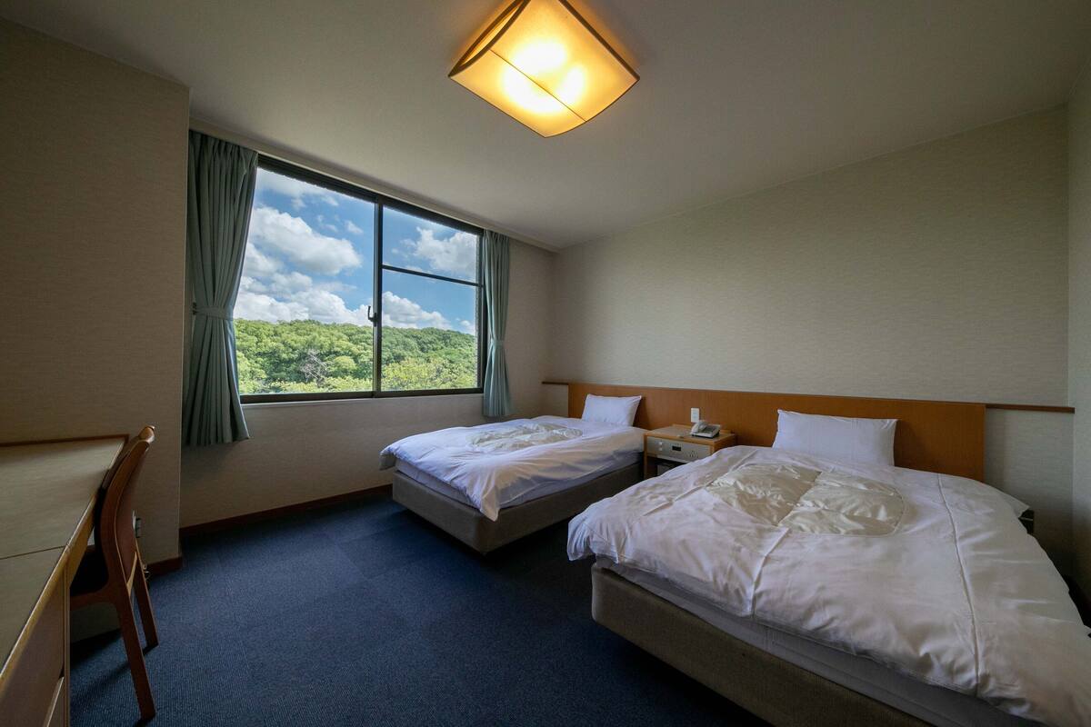 Une chambre d’hôtel avec deux lits, un bureau et une fenêtre donnant sur un paysage verdoyant.