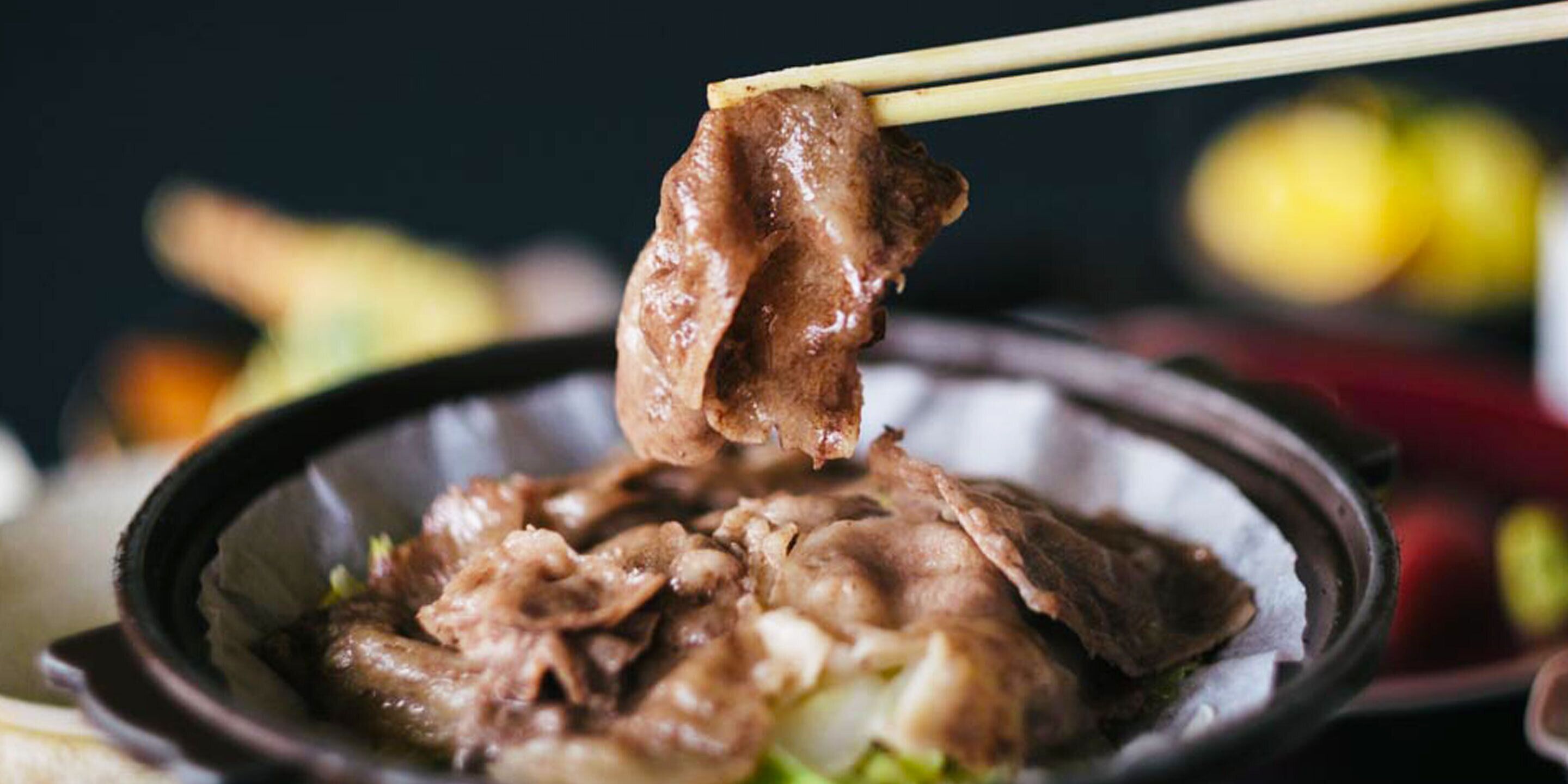 Un plato de comida con palillos levantando un trozo de carne.