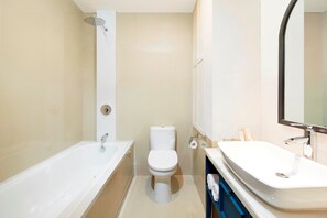 A modern bathroom with a bathtub, toilet, and sink. - Jambuluwuk Thamrin Hotel (Jakarta)