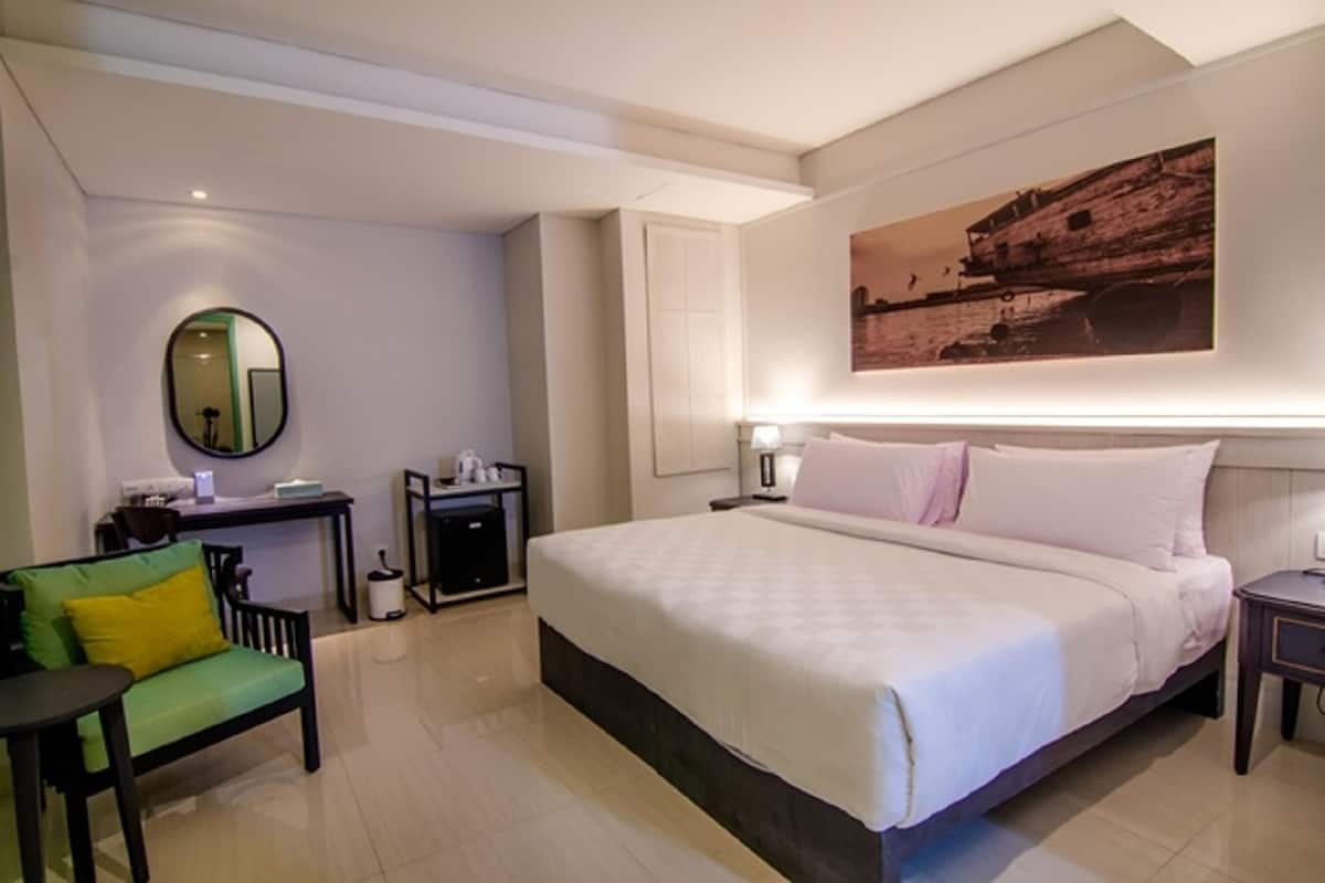 A hotel room with a bed, a desk, a chair, a mirror, and a wall-mounted artwork.
