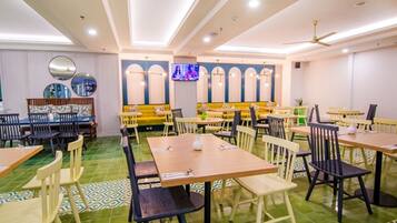 Un restaurante con varias mesas y sillas, una pantalla de televisión y un ventilador de techo.