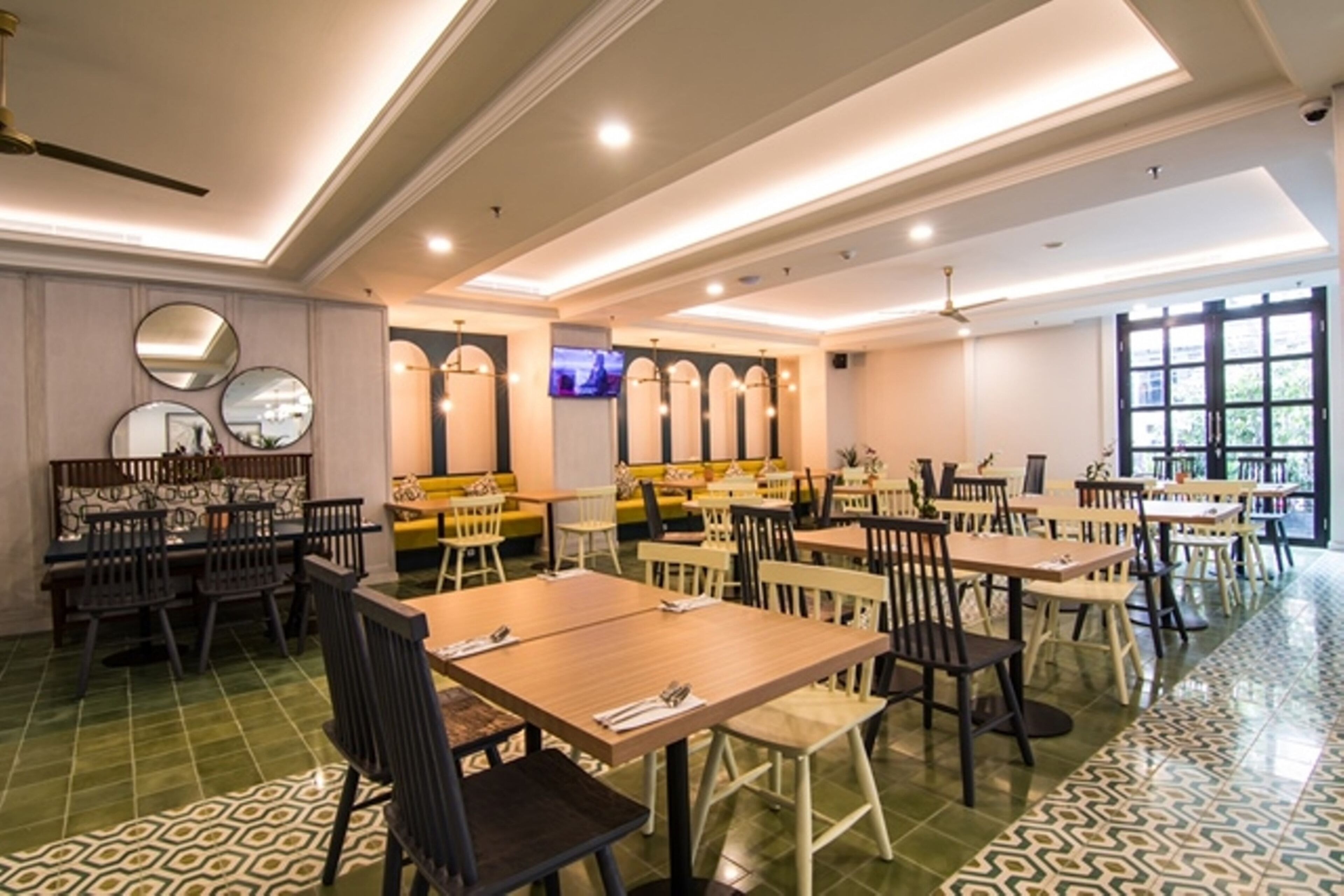 A spacious restaurant with multiple tables and chairs, a ceiling fan, and a television on the wall.