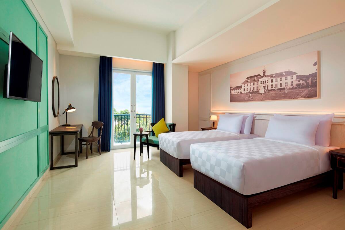 A hotel room with two beds, a desk, a chair, a TV, and a balcony with a view.
