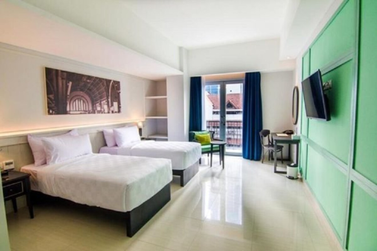 Habitación de hotel con dos camas, un escritorio, una silla, un televisor y una ventana con cortinas.