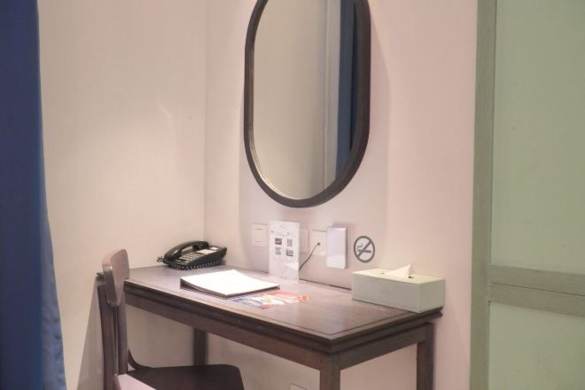 Una habitación de hotel con escritorio, teléfono, caja de pañuelos y un espejo montado en la pared.