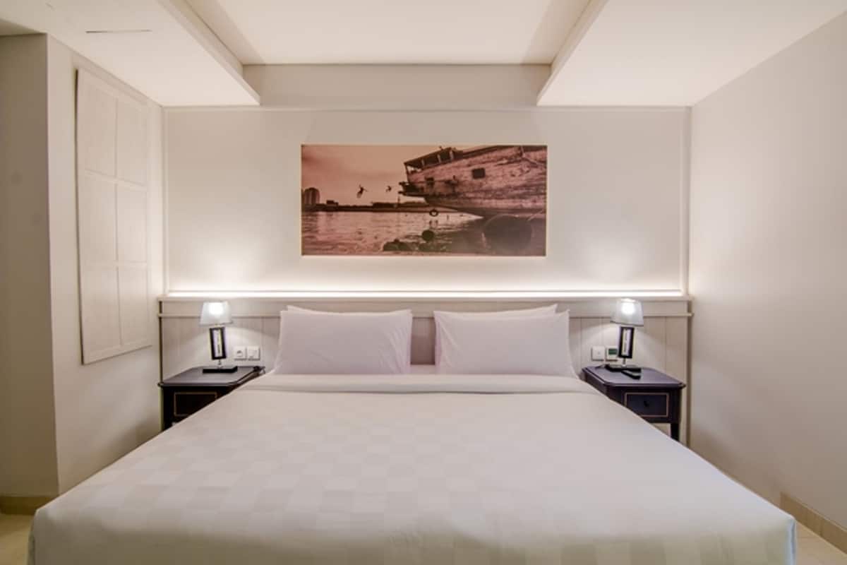 A hotel room with a large bed, two bedside tables with lamps, and a wall-mounted painting of a coastal scene.