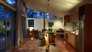 A modern kitchen with a large island, wooden flooring, and a view of the outdoors through large windows.