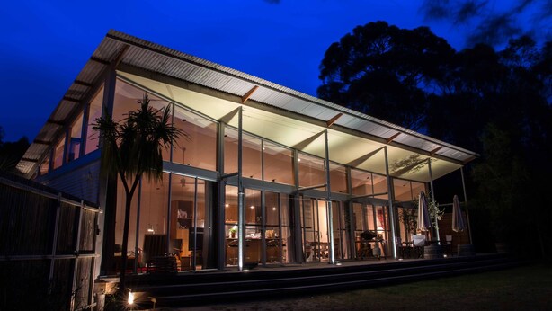 A modern house with large glass windows, a covered patio, and a well-lit interior.