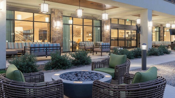An outdoor seating area with wicker furniture and a fire pit, surrounded by stone pillars and glass doors leading to indoor spaces. - Courtyard by Marriott Thousand Oaks Agoura Hills (Agoura Hills)