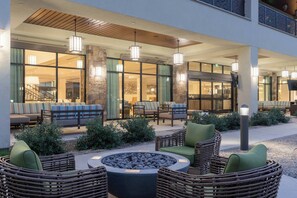 An outdoor seating area with wicker furniture and a fire pit, surrounded by stone pillars and glass doors leading to indoor spaces. - Courtyard by Marriott Thousand Oaks Agoura Hills (Agoura Hills)