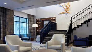 A spacious lobby with a grand staircase, comfortable seating, and a large window offering a view of the outdoors. - Courtyard by Marriott Thousand Oaks Agoura Hills (Agoura Hills)