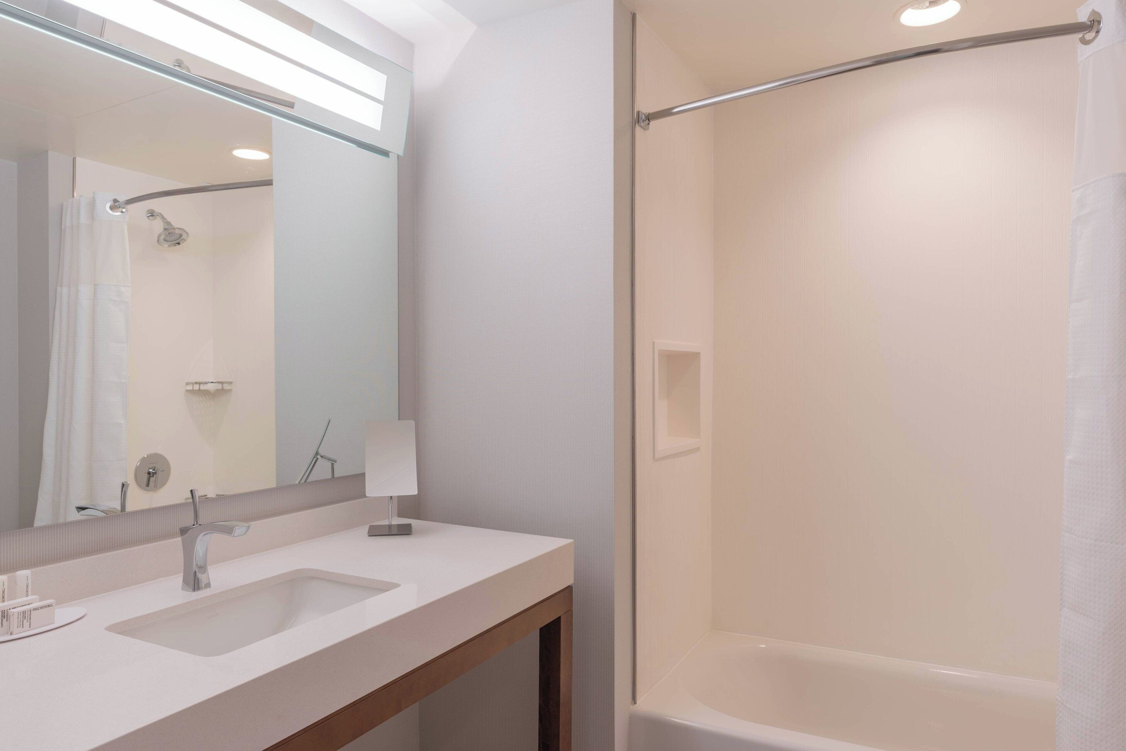 A modern bathroom with a large mirror, two sinks, a shower, and a towel rack.