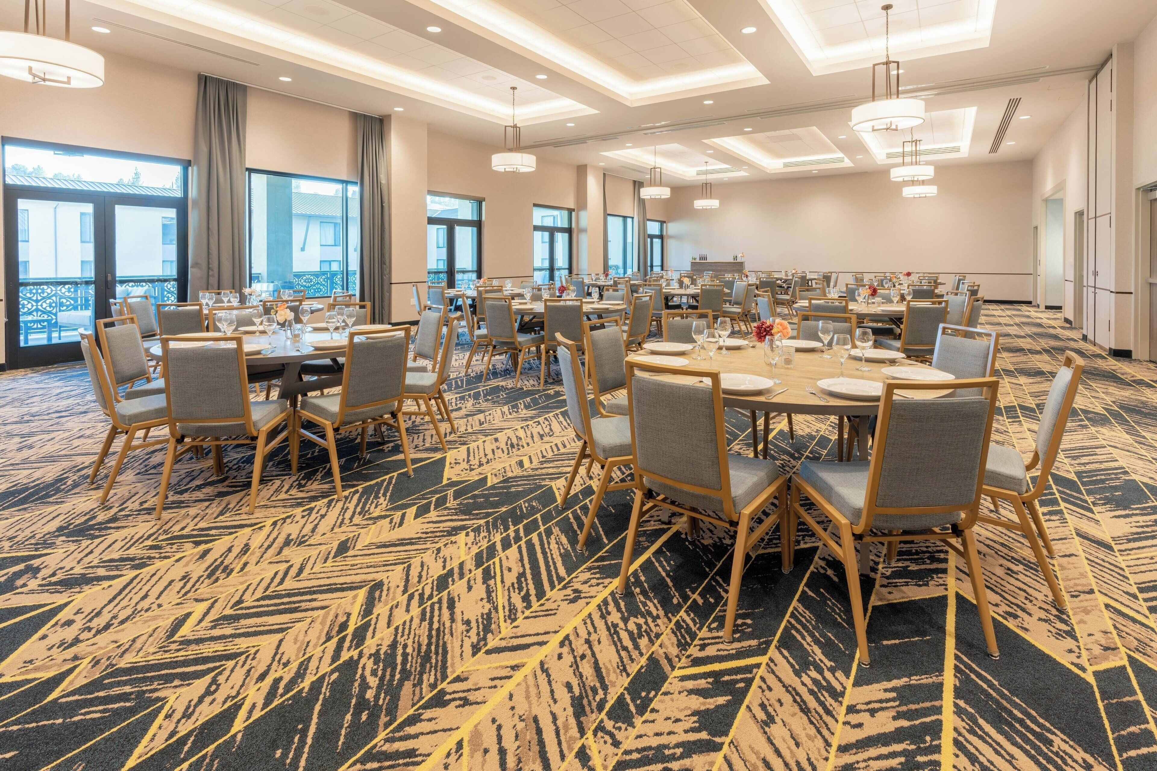 Une salle de conférence spacieuse, dotée de plusieurs tables et chaises, de grandes fenêtres et d’un tapis à motifs.