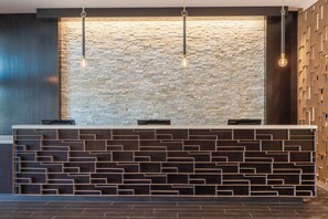 A reception desk with a stone wall backdrop, a modern design with geometric patterns, and hanging pendant lights. - Courtyard by Marriott Thousand Oaks Agoura Hills (Agoura Hills)