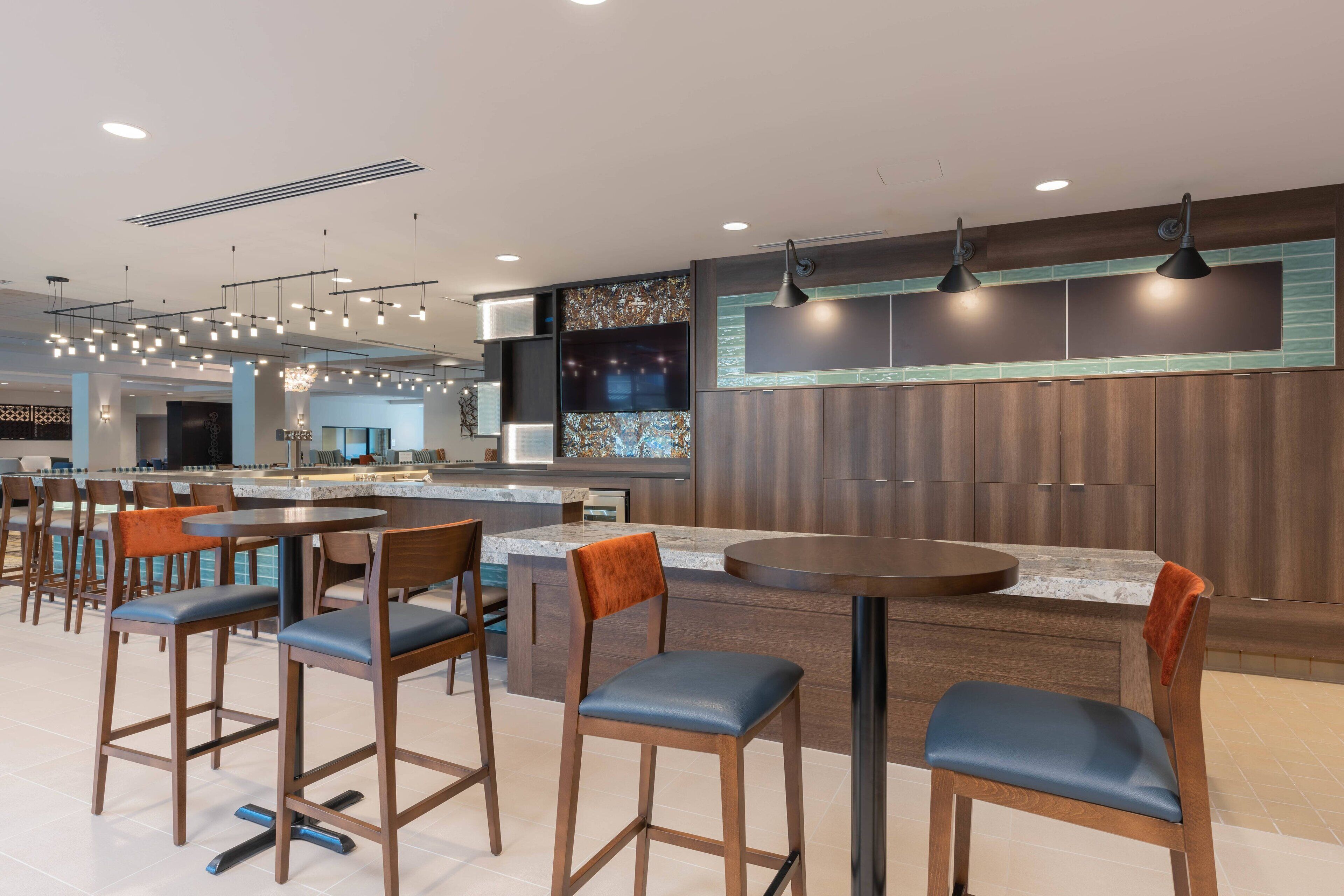 A modern restaurant with a bar area, multiple seating options, and a large kitchen in the background.
