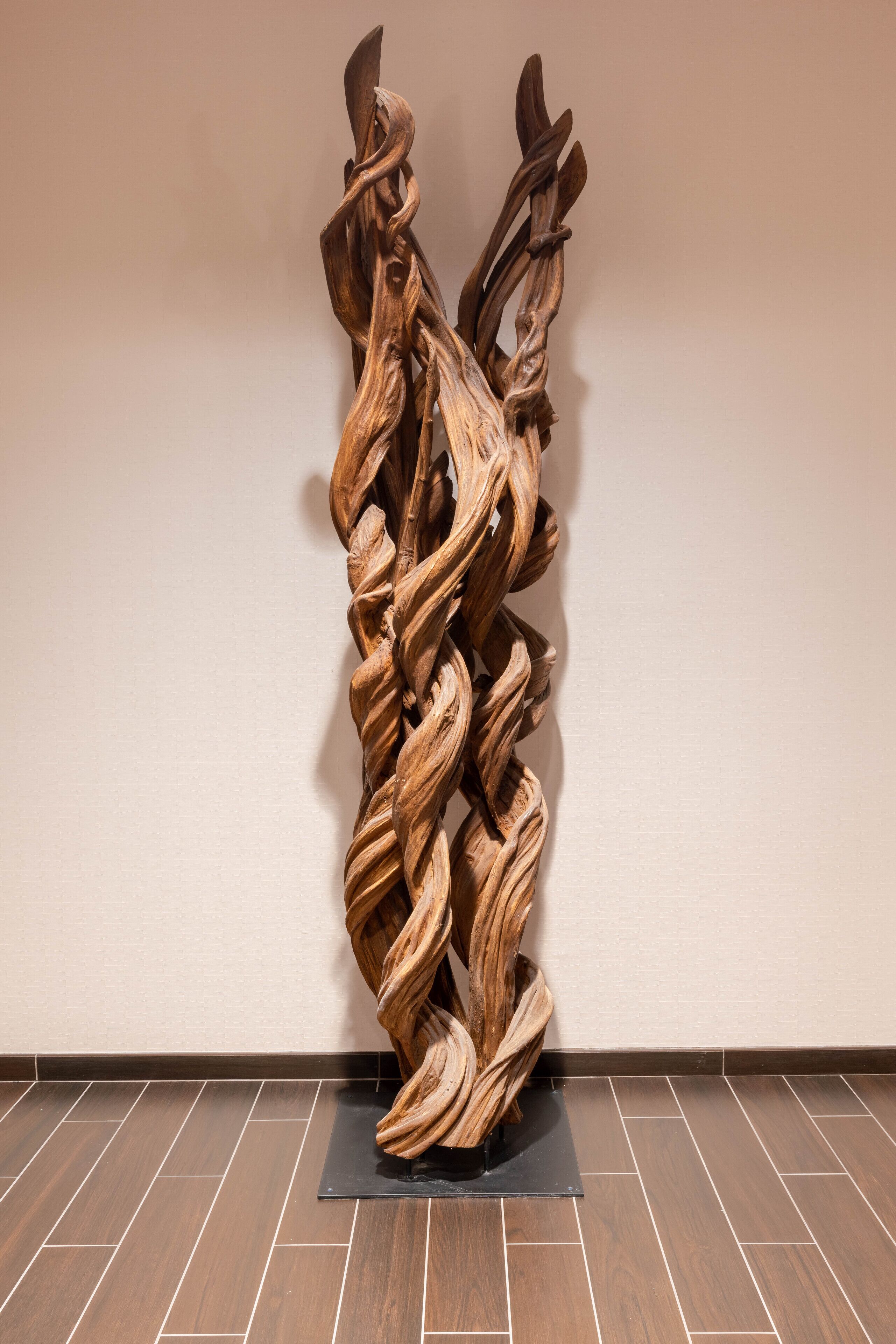 A wooden sculpture on a black base against a plain wall.