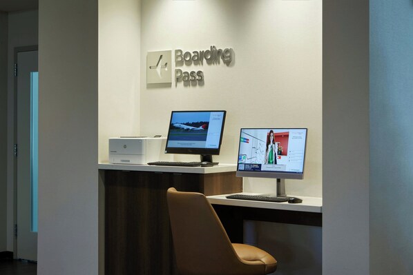 Una recepción con un cartel que dice 'Boarding Pass', dos monitores de computadora, una impresora y una silla marrón.