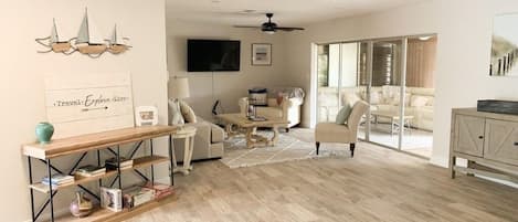A spacious living room with a wooden floor, a sofa set, a coffee table, and a bookshelf.