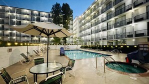 A hotel pool area with lounge chairs, a table, and a covered seating area. - Glendale Express Hotel (Glendale)