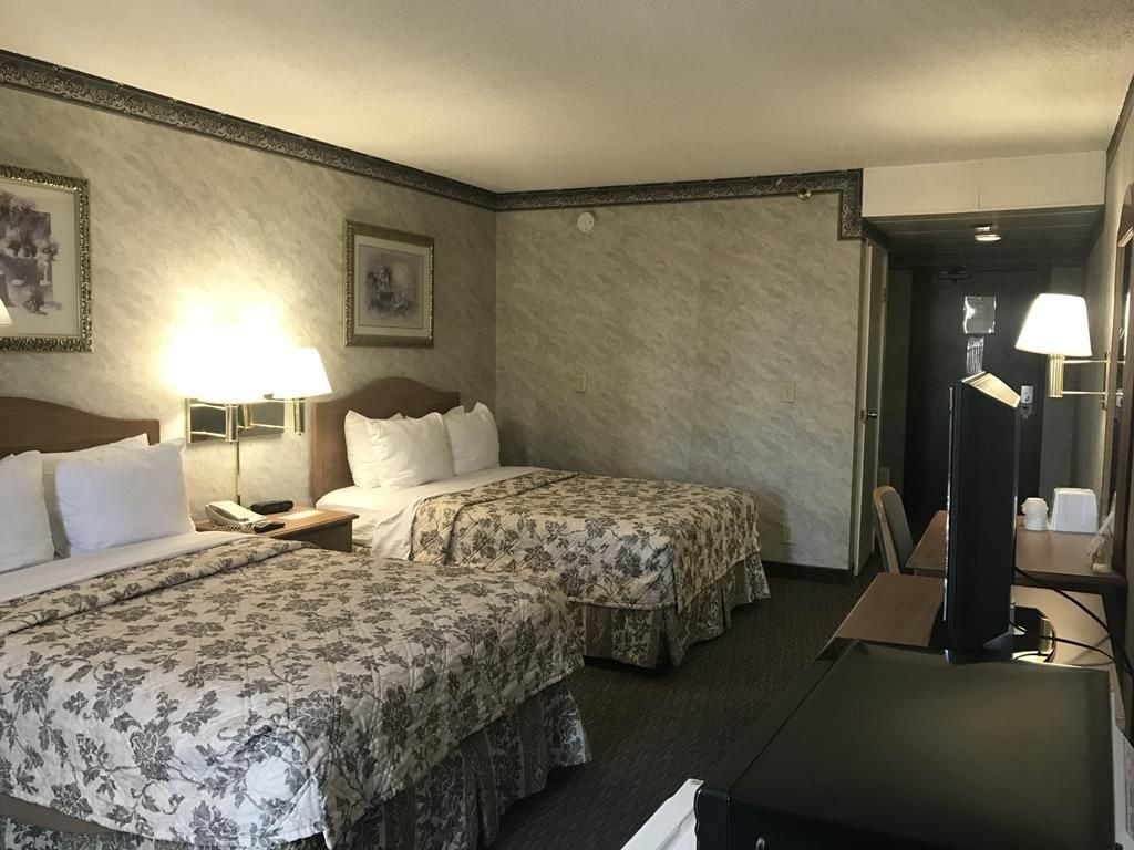 Habitación de hotel con dos camas, un escritorio, una silla, una lámpara y un espejo.