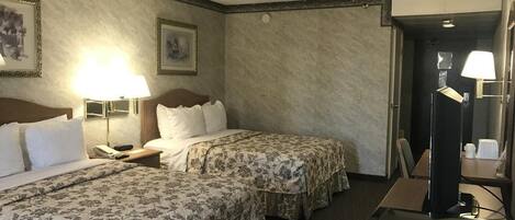 Habitación de hotel con dos camas, un escritorio, una silla, una lámpara y un espejo.