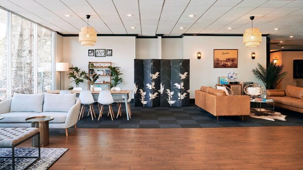 A modern hotel lobby with a seating area, a dining table, and a decorative screen. - Glendale Express Hotel (Glendale)