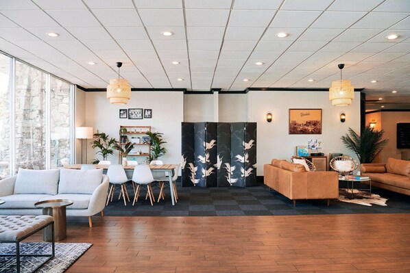 A modern hotel lobby with a seating area, a dining table, and a decorative screen.