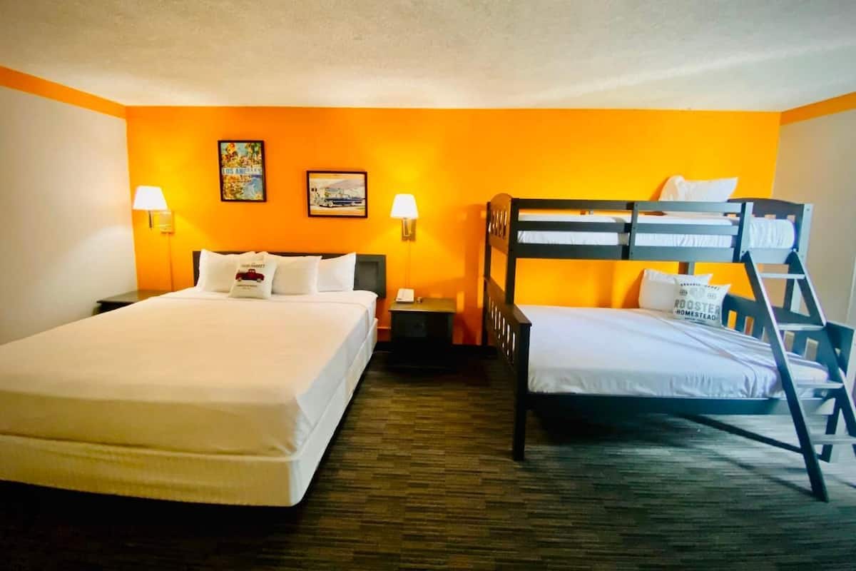 A hotel room with two beds, one double and one bunk, a nightstand, a lamp, and two wall-mounted lamps.