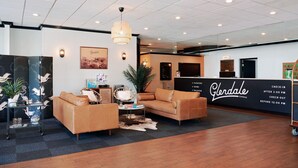 A hotel lobby with a reception desk, two sofas, a coffee table, a potted plant, and a wall-mounted light fixture. - Glendale Express Hotel (Glendale)