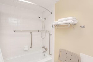 A bathroom with a white bathtub, grab bars, a shelf with towels, and a white toilet.