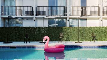 A swimming pool with a pink flamingo float, a hedge, and a building with balconies.