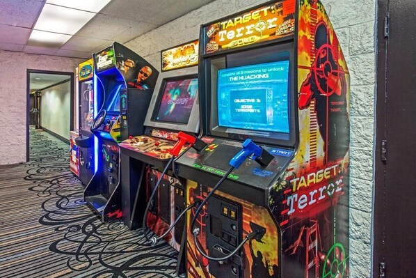 A row of arcade gaming machines with 'Target Terror' branding, connected to a power source, in a hallway with patterned carpet.