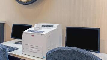 Ein Schreibtisch mit einem Drucker, zwei Computermonitoren und einer Uhr an der Wand.