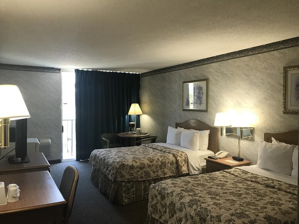 Habitación de hotel con dos camas, un escritorio, una silla, una lámpara, un teléfono y un cuadro en la pared.
