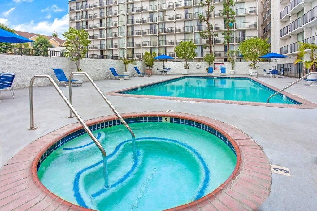 A hotel pool area with two hot tubs and lounge chairs.