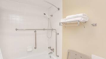 A bathroom with a white bathtub, grab bars, a shelf with towels, and a white toilet.