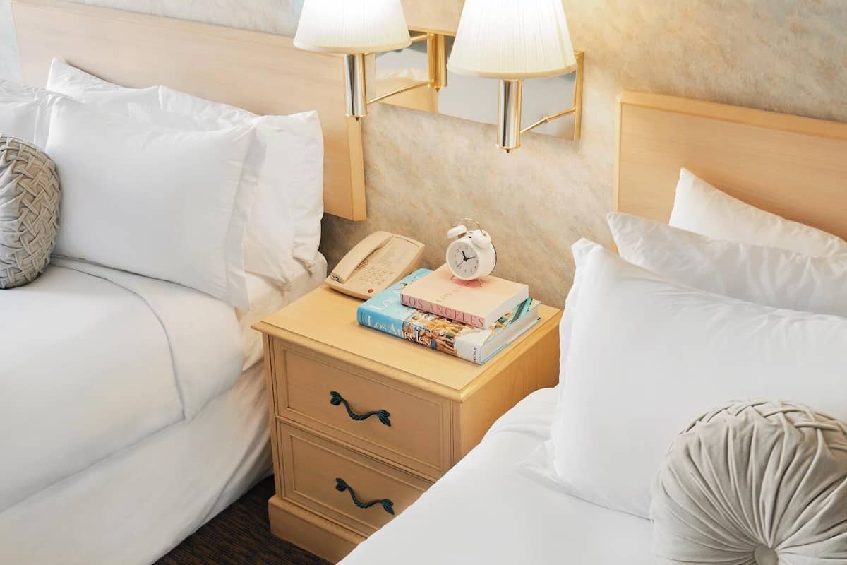 A hotel room with a bed, a nightstand with a lamp, a telephone, a book, and a clock.