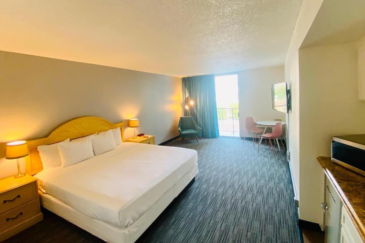 A hotel room with a bed, bedside lamps, a desk, a chair, a television, and a view of the outdoors.
