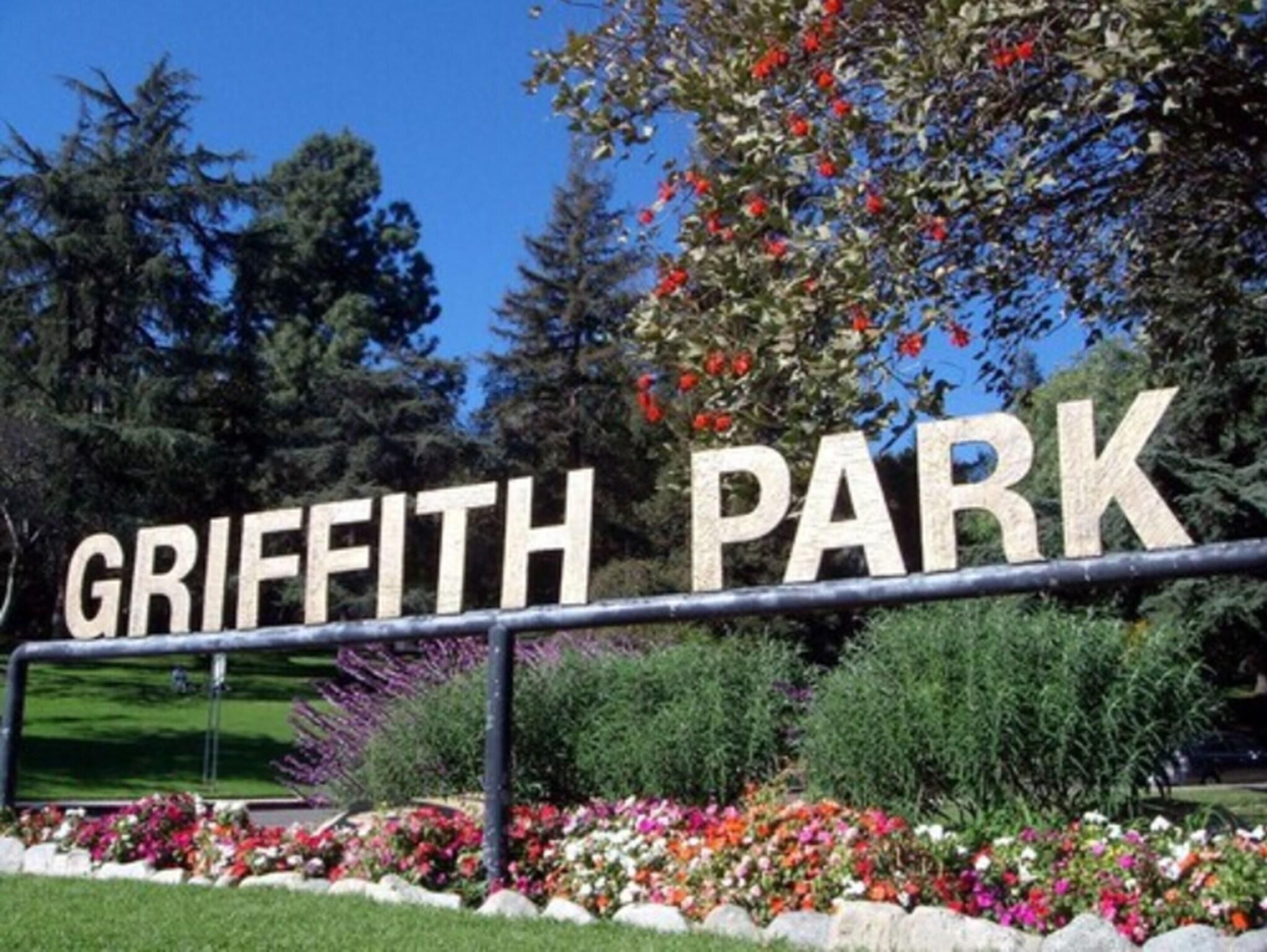 A sign for Griffith Park with a metal fence and flower beds in the foreground.